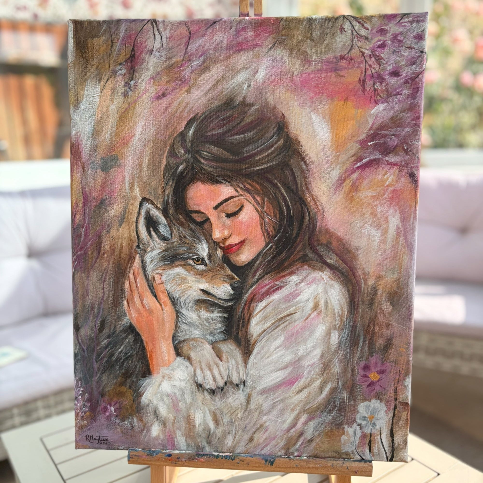 Painting of a woman hugging a wolf on an easel outdoors.