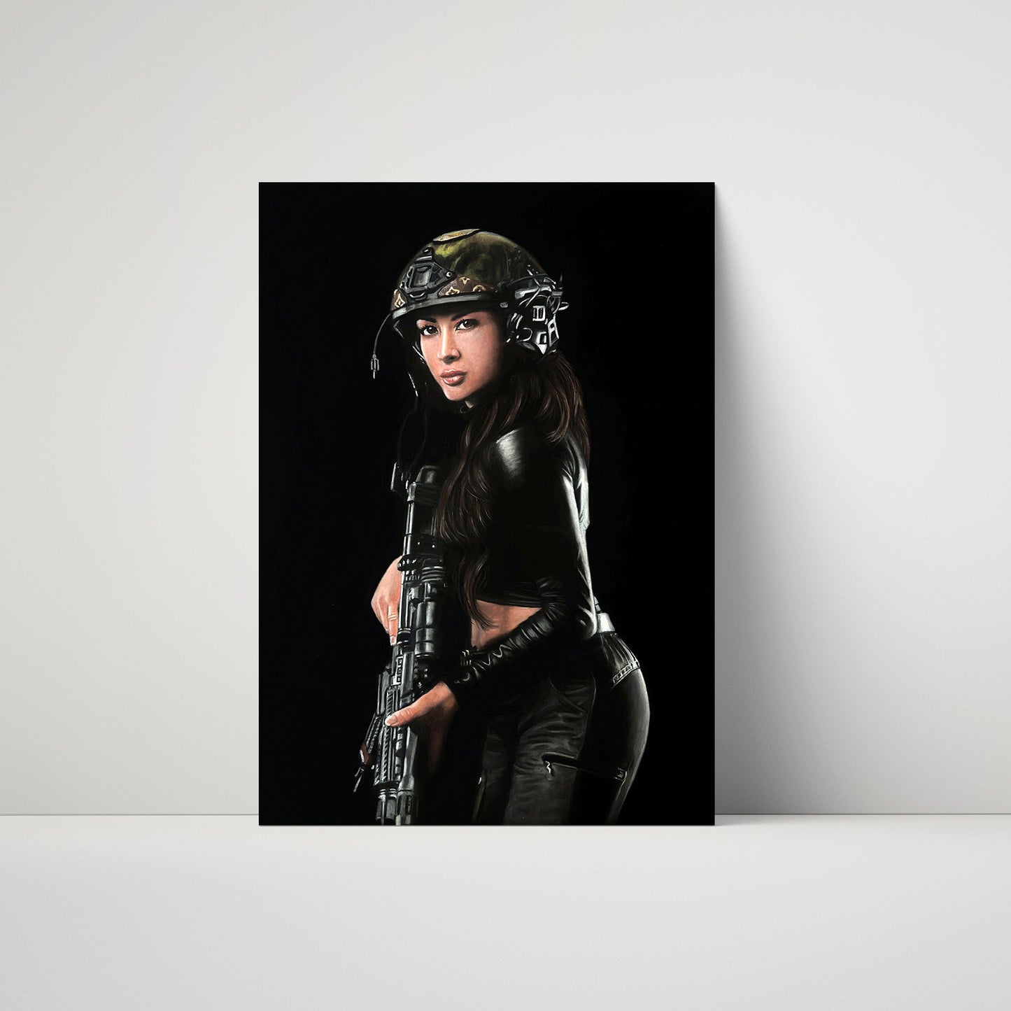 A vertical art print or poster leaning against a light gray wall on a white surface. The print shows a woman in tactical gear and a helmet holding a rifle against a black background.