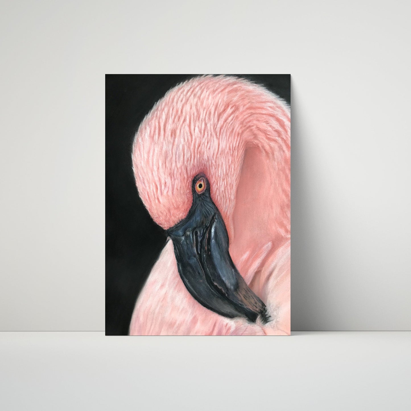 A vertical art print depicting a close-up portrait of a pink flamingo with a black beak against a dark background, leaning against a light gray wall on a white surface.