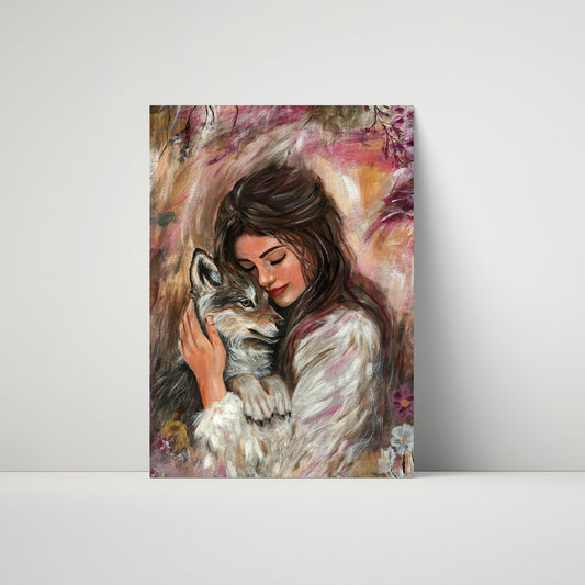 A vertical art print or canvas leaning against a light gray wall on a white surface. The artwork depicts a woman in a white coat embracing a gray and white wolf, rendered in a soft, painterly style with pink, brown, and cream tones.